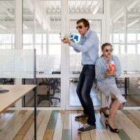 Mann und Frau in formeller Kleidung stehen Rücken an Rücken und zielen auf Nerf Gun Spielzeugpistolen, während sie sich im Büro amüsieren