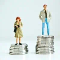 Das Bild stellt einen Mann dar, der auf einem höheren Stapel Geld steht als eine Frau, was symbolisch den Lohnunterschied zwischen den Geschlechtern darstellt.